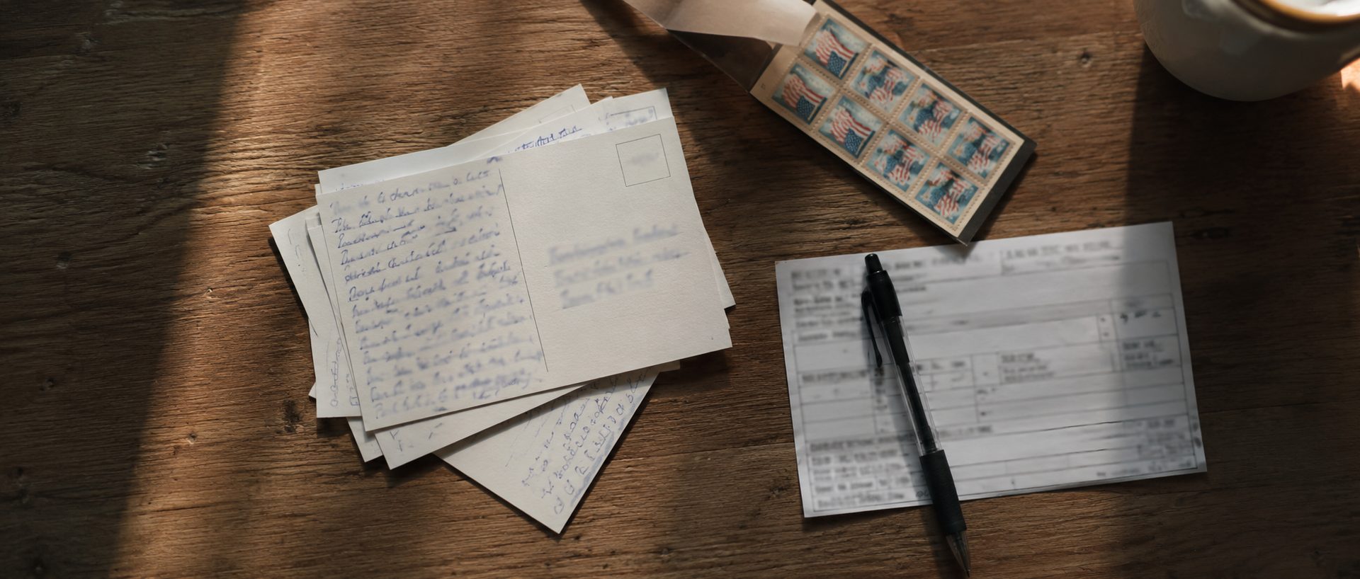 Handwritten postcards, a book of stamps and a commissary deposit slip on a kitchen table, the everyday work of supporting someone in jail.